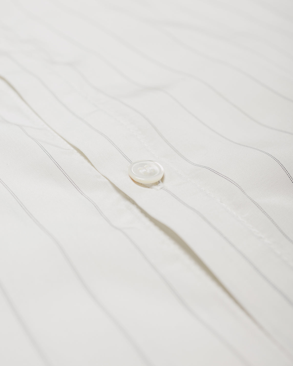Close-up of a white button-up shirt with thin vertical gray pinstripes and a single visible white button on the front placket.