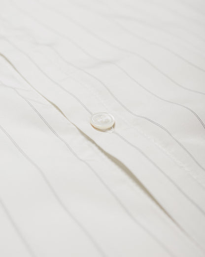 Close-up of a white button-up shirt with thin vertical gray pinstripes and a single visible white button on the front placket.